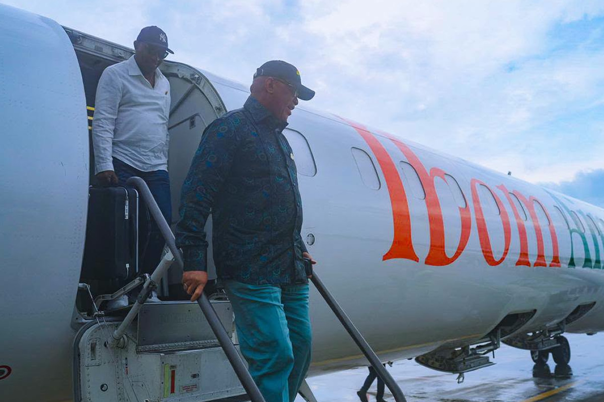Two men stepping off a white aircraft via portable stairs on a tarmac, with orange lettering along the fuselage.