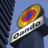 Oando sign: a circular multicolor logo above the word 'Oando' on a white panel against a blue sky.
