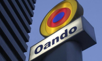 Oando sign: a circular multicolor logo above the word 'Oando' on a white panel against a blue sky.
