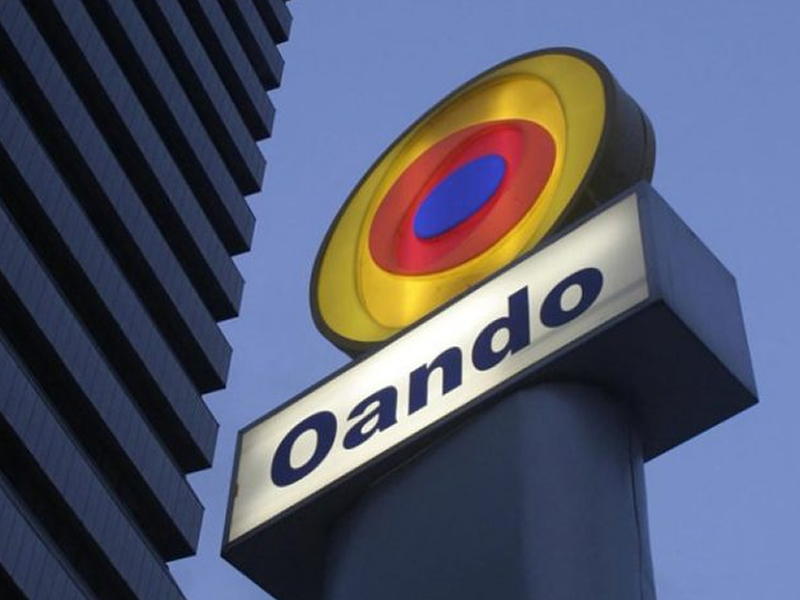 Oando sign: a circular multicolor logo above the word 'Oando' on a white panel against a blue sky.