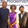 Three people pose for a photo at an art celebration event, with a banner behind them that reads 'Modernism... A Celebration of Art, Legacy'.