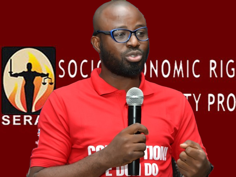 Man with glasses and a beard in a red polo shirt speaking into a handheld microphone on a red backdrop with a logo.