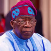 Elderly man in light blue traditional attire and a red-blue patterned cap, sitting indoors.