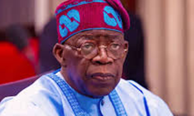 Elderly man in light blue traditional attire and a red-blue patterned cap, sitting indoors.