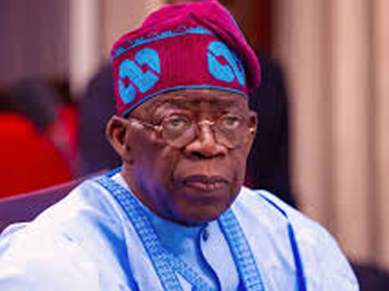 Elderly man in light blue traditional attire and a red-blue patterned cap, sitting indoors.