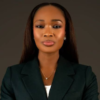 Professional portrait of a woman wearing a dark green blazer, pearl earrings, and a necklace, against a neutral backdrop.