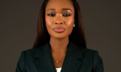 Professional portrait of a woman wearing a dark green blazer, pearl earrings, and a necklace, against a neutral backdrop.