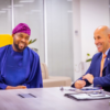 Two men sit at a conference table in an office, smiling and talking.