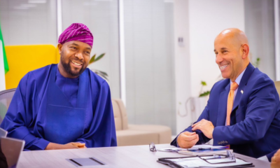 Two men sit at a conference table in an office, smiling and talking.