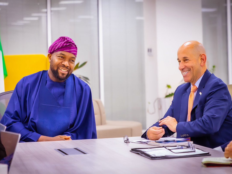 Two men sit at a conference table in an office, smiling and talking.
