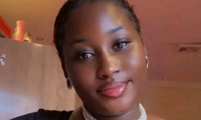 Portrait of a young woman with short hair, wearing a pearl choker and hoop earrings, indoors with warm lighting.