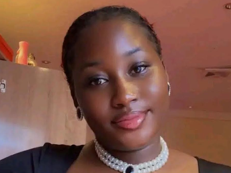 Portrait of a young woman with short hair, wearing a pearl choker and hoop earrings, indoors with warm lighting.