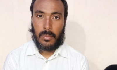 Portrait of a man with short dark hair and a full beard, wearing a white button-down shirt, looking at the camera.