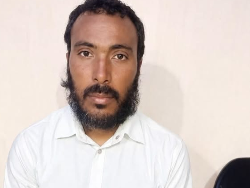 Portrait of a man with short dark hair and a full beard, wearing a white button-down shirt, looking at the camera.