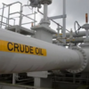 Large oil transport pipeline at an industrial facility with a bright yellow 'CRUDE OIL' label and visible valves.