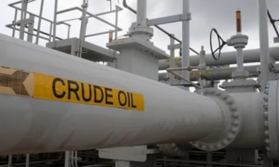 Large oil transport pipeline at an industrial facility with a bright yellow 'CRUDE OIL' label and visible valves.