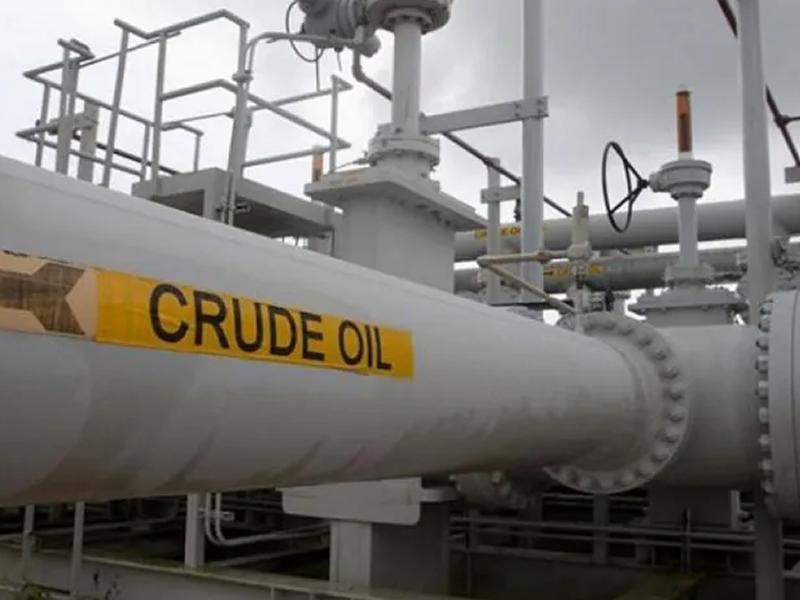 Large oil transport pipeline at an industrial facility with a bright yellow 'CRUDE OIL' label and visible valves.