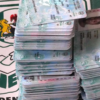 Two tall stacks of Nigerian 100-naira banknotes on a table beside an INEC banner.