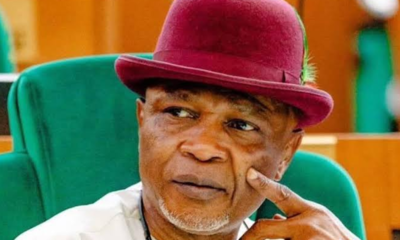 Portrait of an older man wearing a burgundy hat, seated in a green chair, looking pensively to the side.