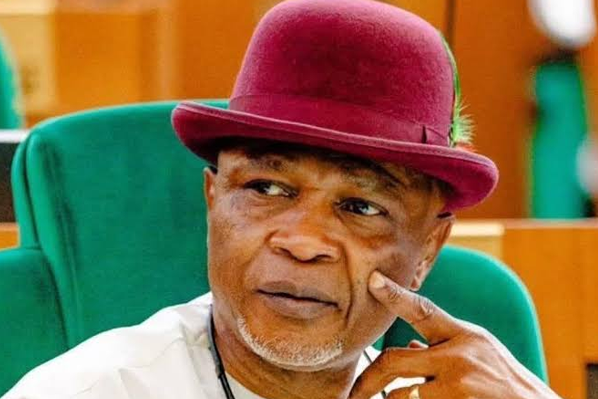 Portrait of an older man wearing a burgundy hat, seated in a green chair, looking pensively to the side.