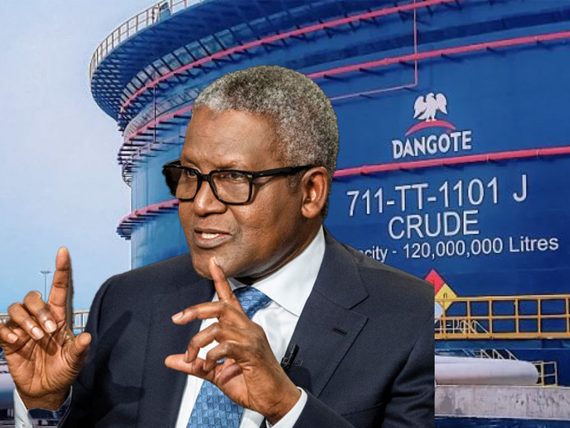 Businessman wearing glasses in a dark suit and blue tie gestures while speaking, with a large Dangote crude oil storage tank in the background.
