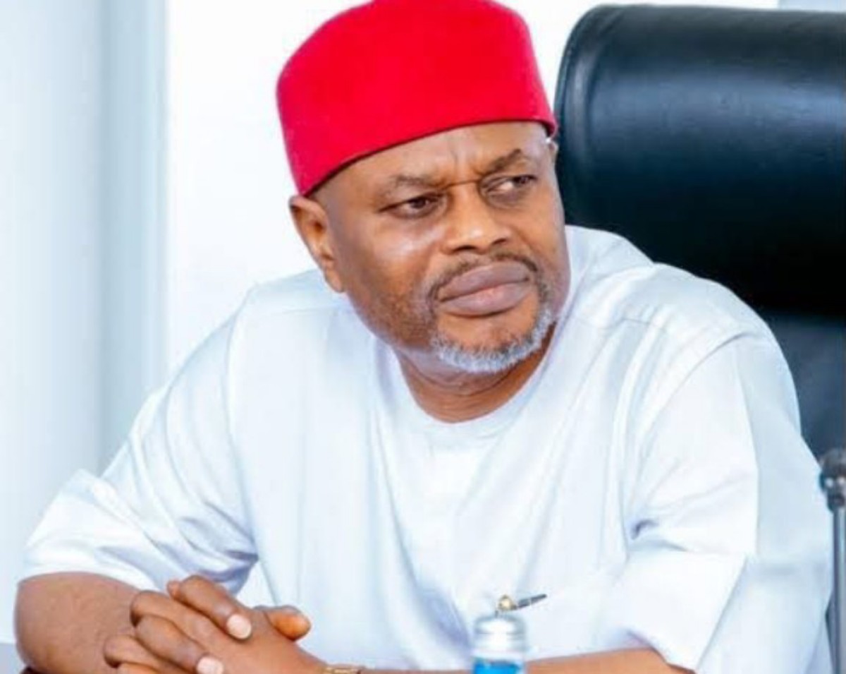A man wearing a red fez and white traditional attire sits at a desk, looking to his left with a thoughtful, concerned expression.