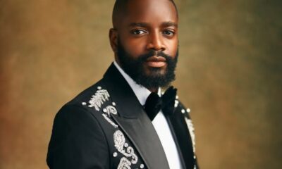 Portrait of a man in a black tuxedo with ornate silver embroidery, white shirt and bow tie, posed against a warm brown studio backdrop.