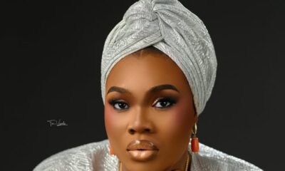 Portrait of a woman with a silver patterned headwrap and matching outfit, wearing gold earrings against a dark backdrop.