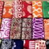 Assorted folded batik fabrics with bright floral and geometric patterns arranged in a grid on the floor.