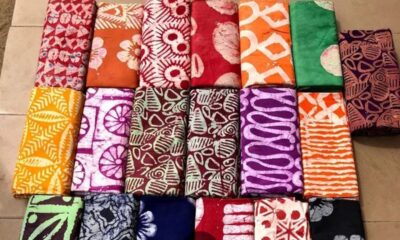 Assorted folded batik fabrics with bright floral and geometric patterns arranged in a grid on the floor.