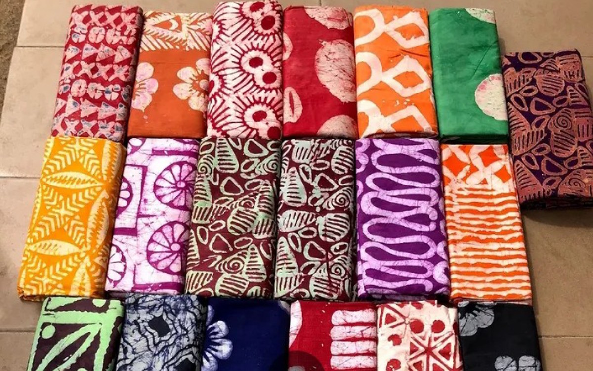 Assorted folded batik fabrics with bright floral and geometric patterns arranged in a grid on the floor.