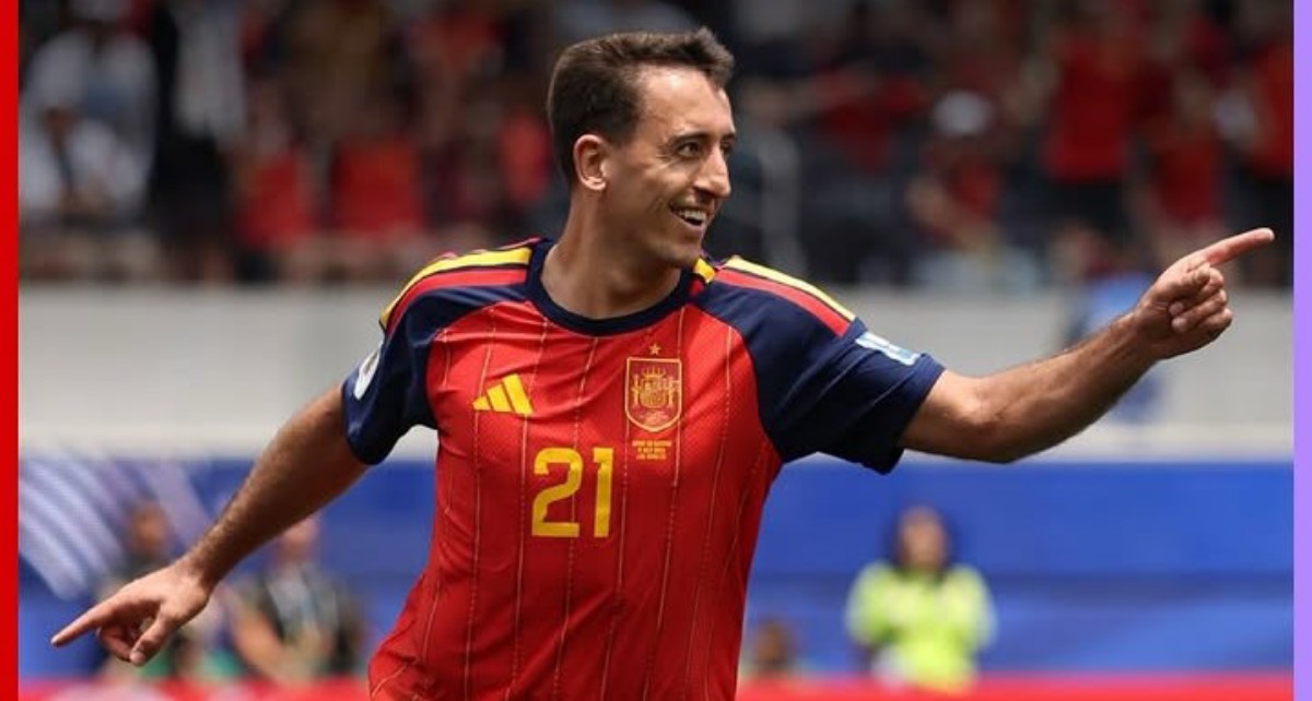 Soccer player in a red Spain jersey #21 celebrates on the field, pointing with his right arm toward the right side.