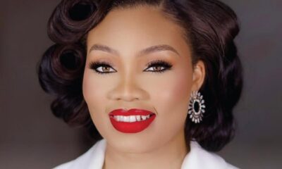 Close-up of a smiling woman with vintage curls, bold red lips, dramatic eyeliner, and sparkly earrings.