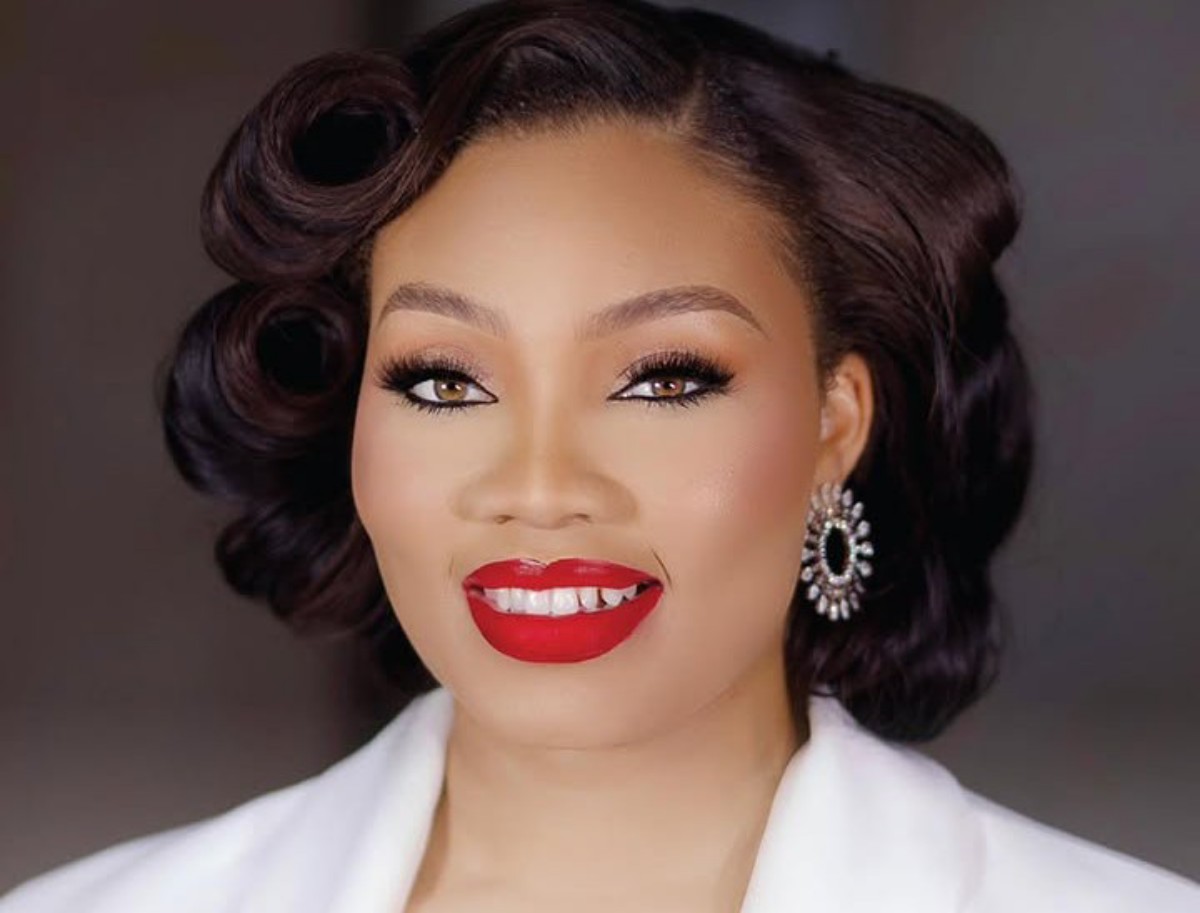 Close-up of a smiling woman with vintage curls, bold red lips, dramatic eyeliner, and sparkly earrings.
