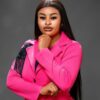Professional woman in a bright pink blazer, posed with chin resting on her hand against a gray studio background.