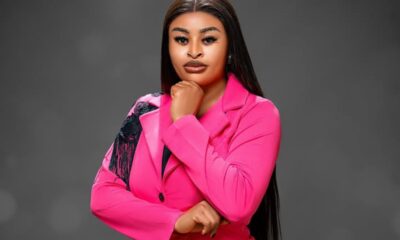 Professional woman in a bright pink blazer, posed with chin resting on her hand against a gray studio background.