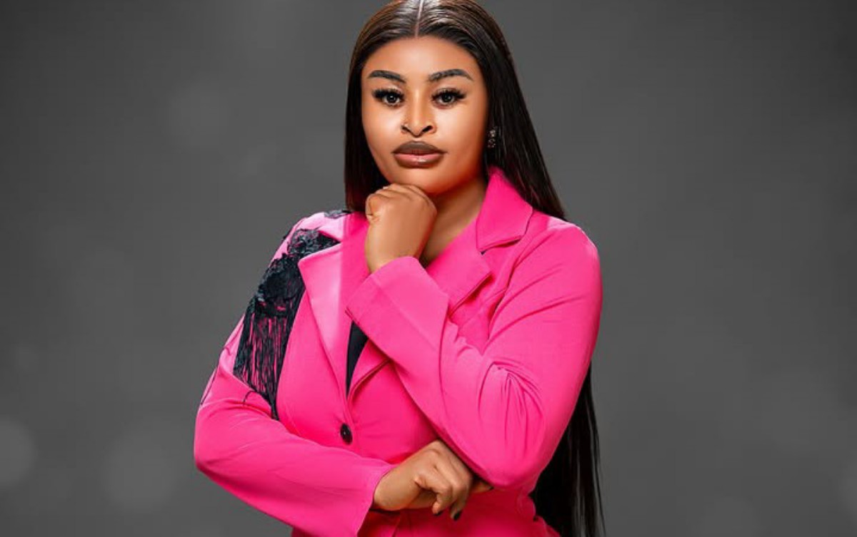 Professional woman in a bright pink blazer, posed with chin resting on her hand against a gray studio background.