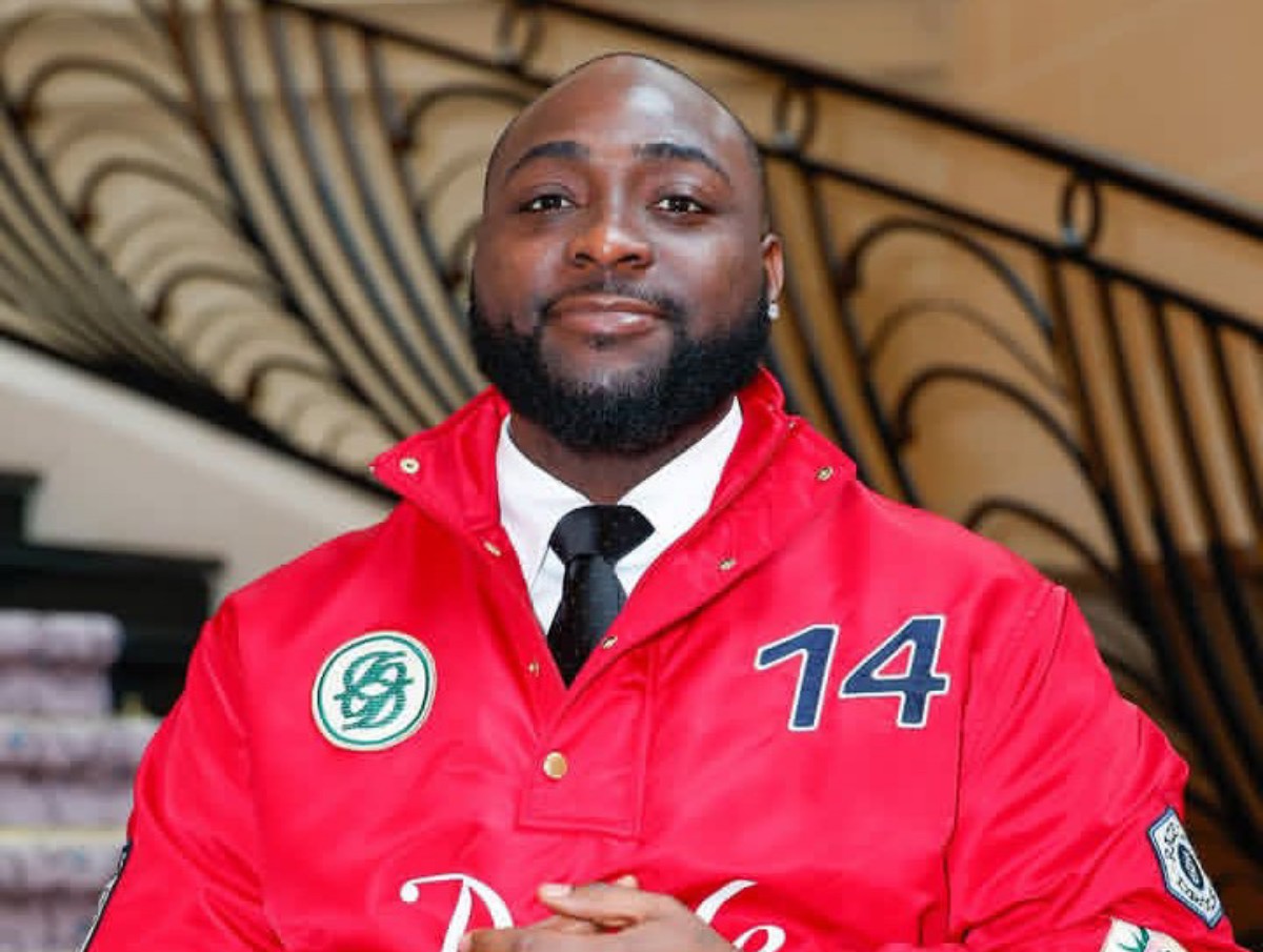 Portrait of a man with a beard wearing a red jacket with the number 14, a white shirt, and black tie, indoors by a curved railing.