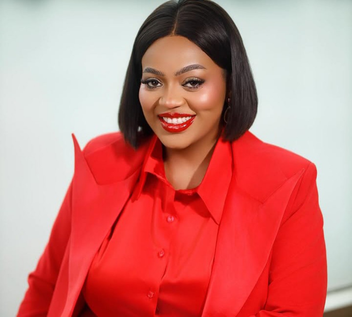 Smiling woman with a black bob haircut wearing a red blazer and blouse against a light background photographed for a professional headshot.