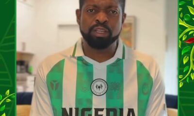Man with beard wearing a Nigeria national football team jersey indoors, looking at the camera.