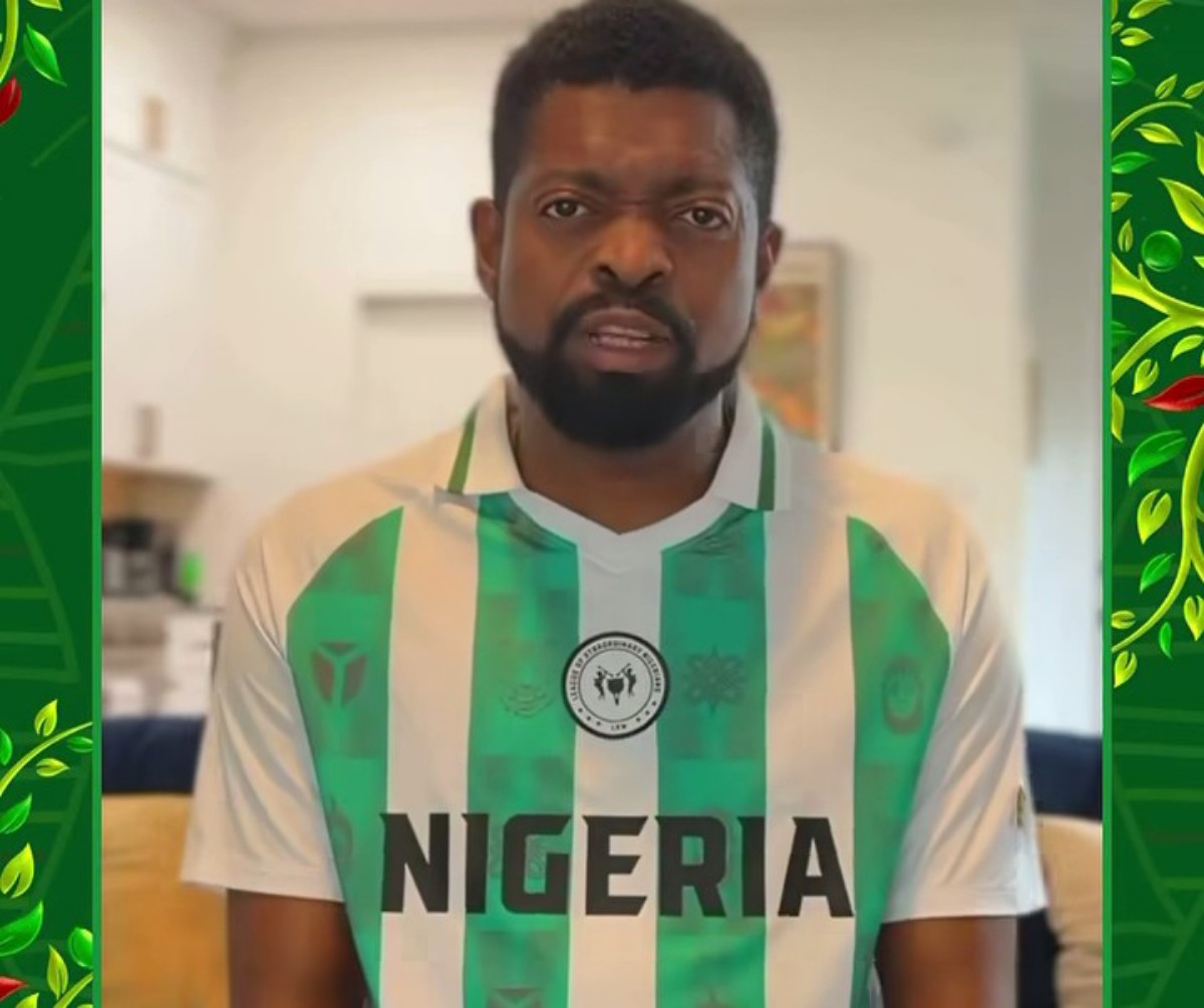 Man with beard wearing a Nigeria national football team jersey indoors, looking at the camera.