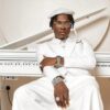 Portrait of a man in an all-white suit and hat, wearing glasses and jewelry, seated at a white piano.
