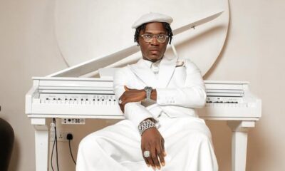 Portrait of a man in an all-white suit and hat, wearing glasses and jewelry, seated at a white piano.
