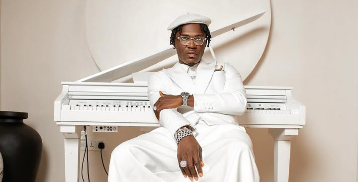 Portrait of a man in an all-white suit and hat, wearing glasses and jewelry, seated at a white piano.