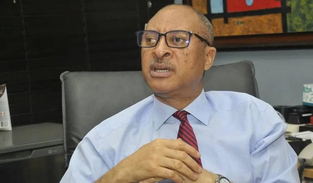Professional man in a light blue shirt and red striped tie sits in an office chair, hands clasped as he speaks.
