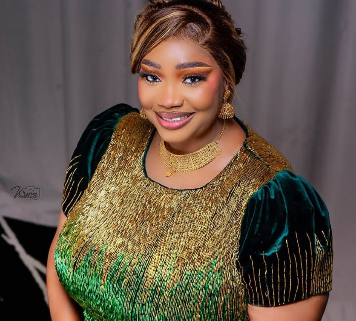 Smiling woman in a gold-and-green sequin dress with matching gold jewelry during a formal photoshoot