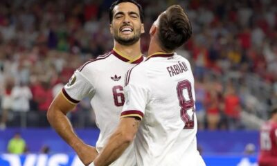 Two male soccer players in white jerseys celebrate on the pitch; numbers 6 and 8 with 'Fabian' on the back.