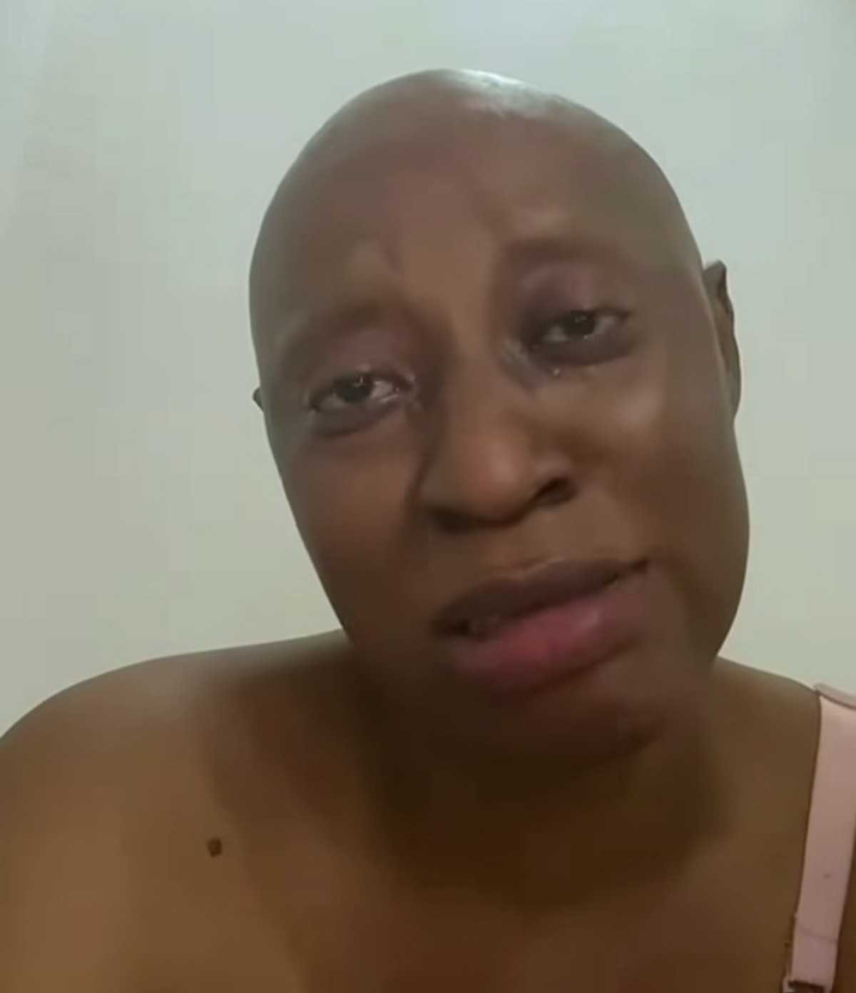 Close-up of a person with a shaved head looking at the camera, wearing a pink sleeveless top, with a calm expression.
