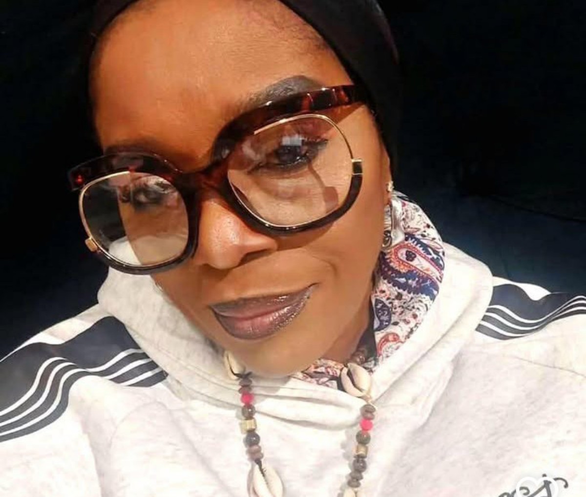 Close-up portrait of a woman wearing oversized round glasses, a head scarf, and a beaded necklace.