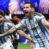 Two Argentina national team football players celebrate on the pitch, arms raised and shouting in blue-and-white striped jerseys with the number 10 visible on one shirt.